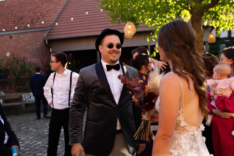 Ein Mann in Anzug, mit Sonnenbrille spricht mit einer Braut